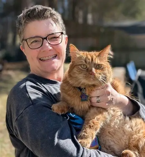 Smiling woman holding a fluffy orange cat.